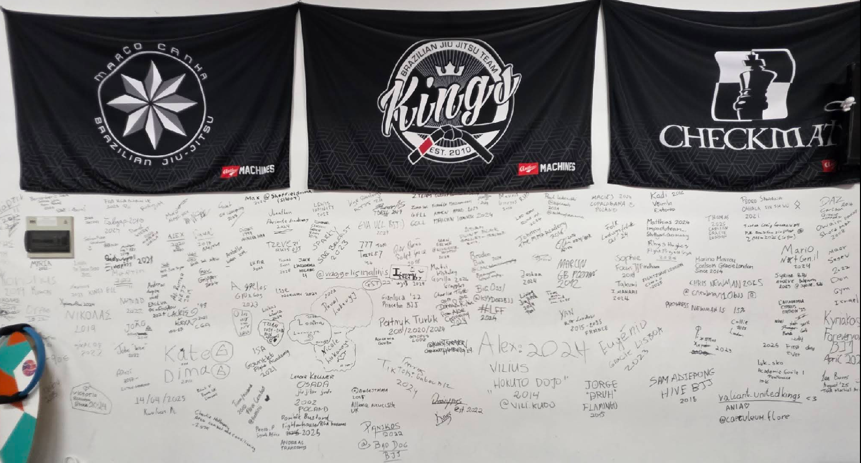 The signature wall by the door, covered in names, belts, and countries from visiting practitioners